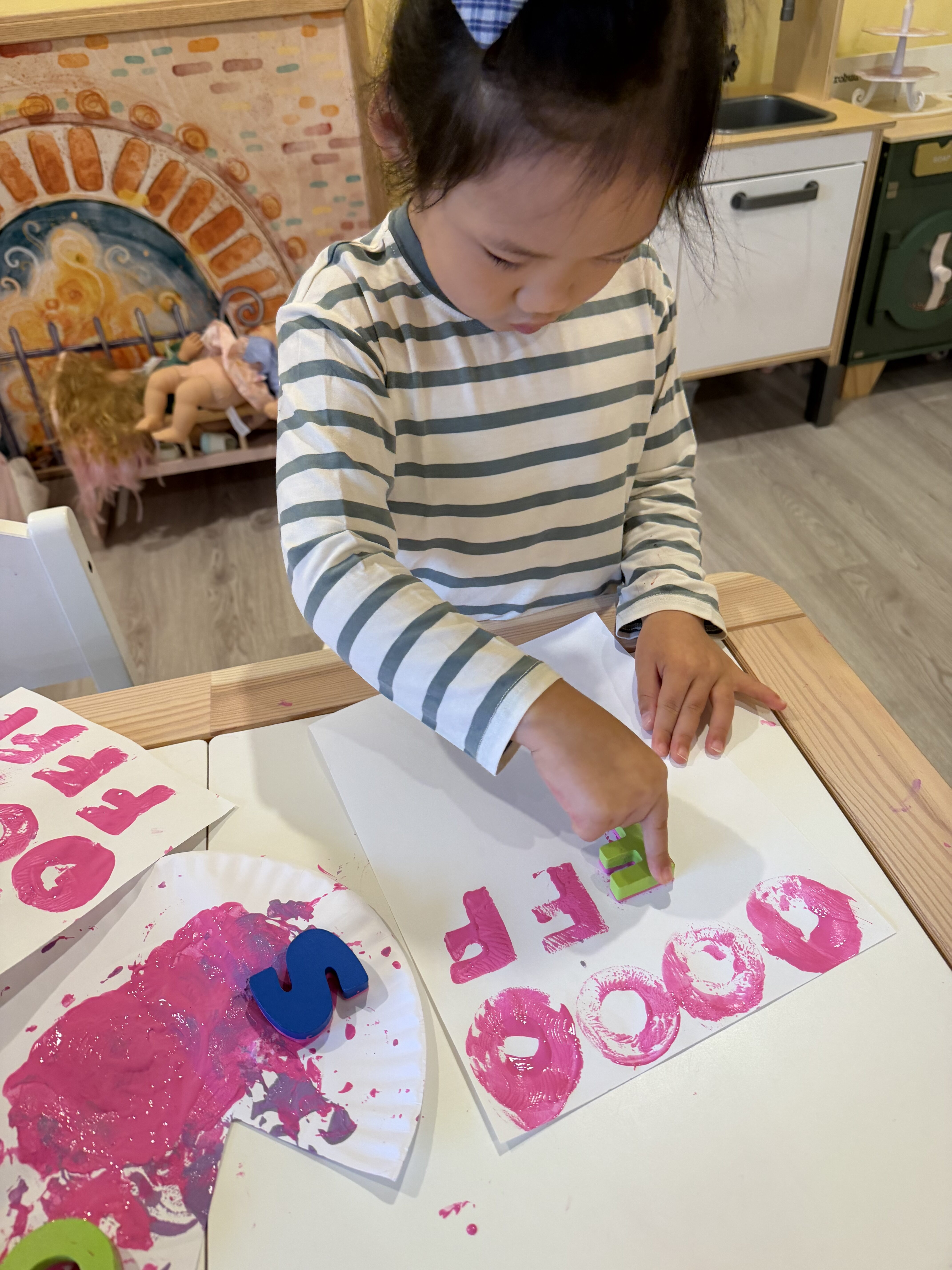 Child stamping letters with pink paint at Kinderly childcare